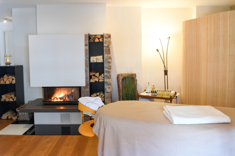 Willkommen bei Massagezeit, Bild der Massageliege in einem gemütlichen Raum mit einem Kaminfeuer